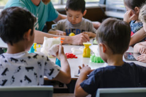 Children sit at a makerspace table and create things with art and science to demonstrate the importance of makerspaces.