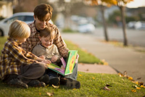Father and sons sitting on the grass, reading a book