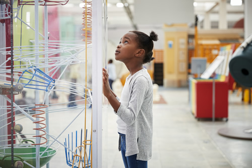 Young girl looking at a science exhibit with a curious expression.
