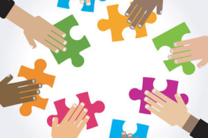 different-colored hands doing a puzzle with assorted colored pieces