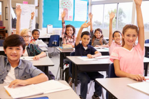 happy elementary school kids raising their hands in a classroom