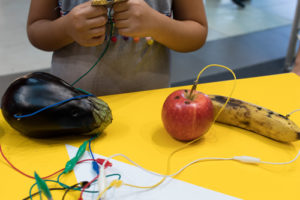Students work on a fruit piano in a school makerspace.