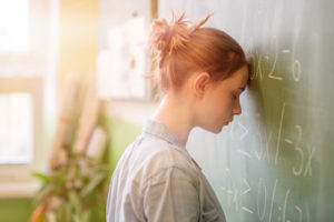 a young girl banging her head against the blackboard in anguish