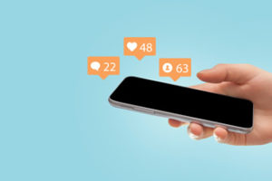 A hand holding a smartphone with social media icons demonstrates the importance of using social media with educators.