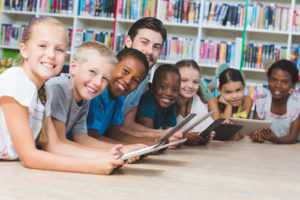 The classroom connectivity gap is closed, and more students than ever have access to robust digital and mobile learning, like these smiling students sitting at a table with their teacher.