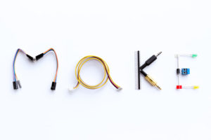 This sign, which says make, is made out of things you would find in a makerspace, like wires and plugs and art supplies.